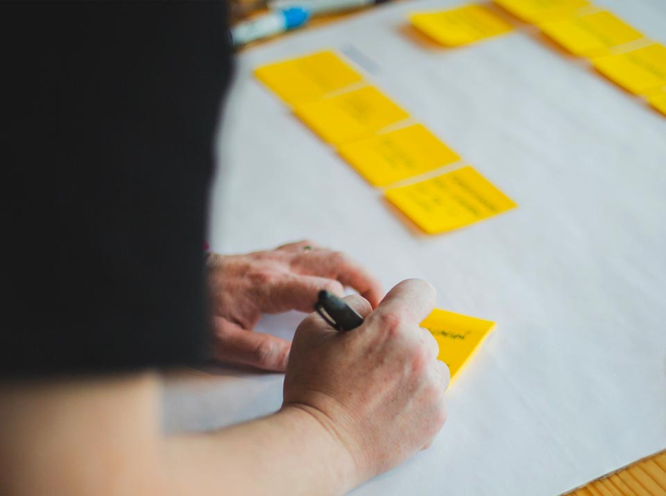 Notizen aus dem Brainstorming auf Post-It schreiben, Mann schreibt Ideen und Ansätze auf kleine Notizzettel, Beschriften von kleinen gelben Klebezetteln während eines Meetings