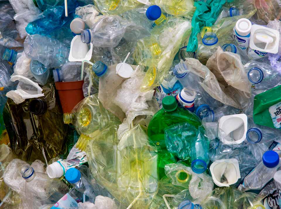 Ansammlung von Plastikflaschen und Joghurtbecher auf einer Recycling Anlage, unsortierte Plastikabfälle mit PET-Flaschen und anderen Kunststoffverpackungen