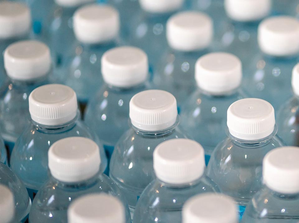 Mineralwasser in recycelten Plastikflaschen mit weißem Schraubverschluss, Nahaufnahme von neuen PET Flaschen mit weißem Deckel aus Recycling Material, Detailaufnahme aus einer Produktionslinie von Getränkeflaschen aus recyceltem Food Grade Material
